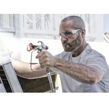 Muž používa striekaciu pištoľ na maliarske práce vonku.