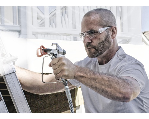 Muž používa striekaciu pištoľ na maliarske práce vonku.