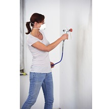 Žena s respirátorom a striekacou pištoľou maľuje stenu