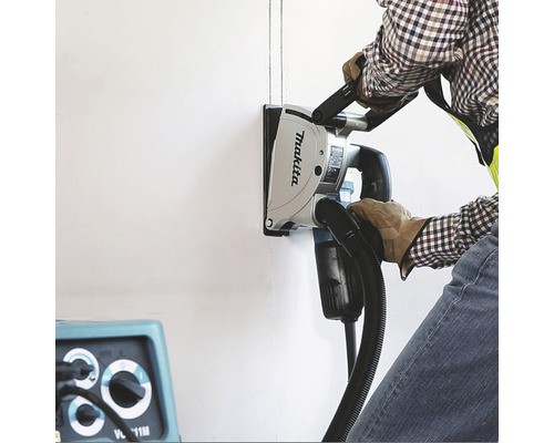 Muž používa drážkovaciu frézu Makita na frézovanie drážok do steny.