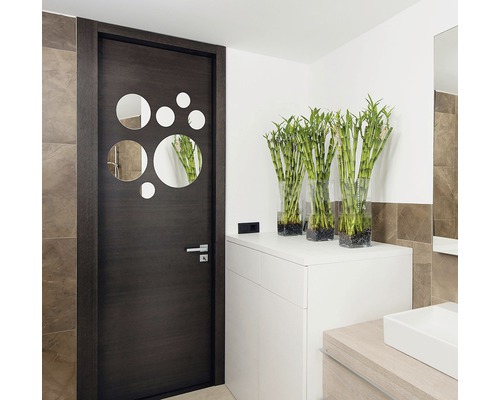 Moderná kúpeľňa s tmavými dverami s kruhovými zrkadlami a bielym nábytkom s bambusovými rastlinami v sklenených vázach.