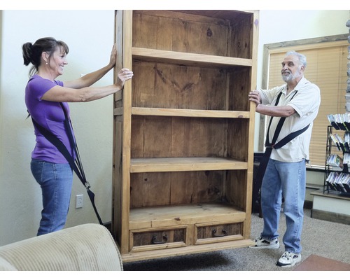 Dve osoby prepravujú drevenú knižnicu pomocou popruhov.