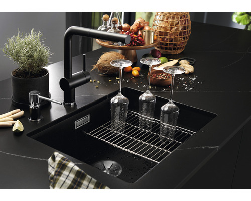 Čierny kuchynský drez s odkvapkávacou mriežkou, batériou a dávkovačom mydla na tmavej pracovnej doske