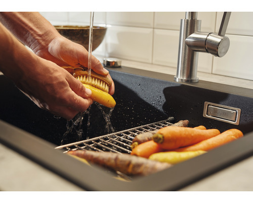 Osoba umýva mrkvu v čiernom dreze s odkvapkávačom pod vodovodnou batériou