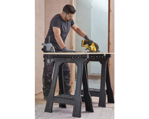 Remeselník reže drevenú dosku na dvoch kozách Stanley v hrubej stavbe.