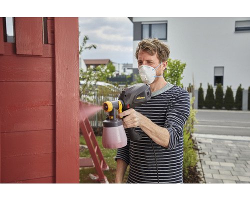 Muž natiera drevo pomocou striekacieho systému a ochrannej masky
