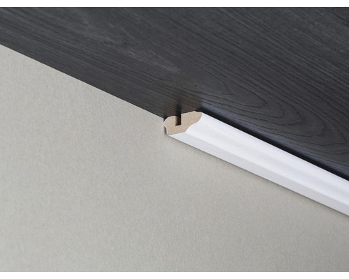 Drevená podlahová lišta pripevnená k stene a tmavej drevenej podlahe