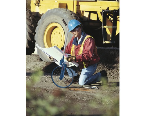 Pracovník so stavebným plánom a meracím kolieskom pred rýpadlom.