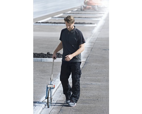 Muž s meracím kolieskom na ceste v pracovnom odeve