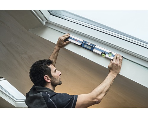 Remeselník používa digitálnu vodováhu na ráme strešného okna.