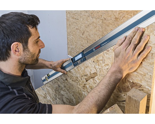 Remeselník meria uhol s digitálnym uhlomerom Bosch na drevenej doske