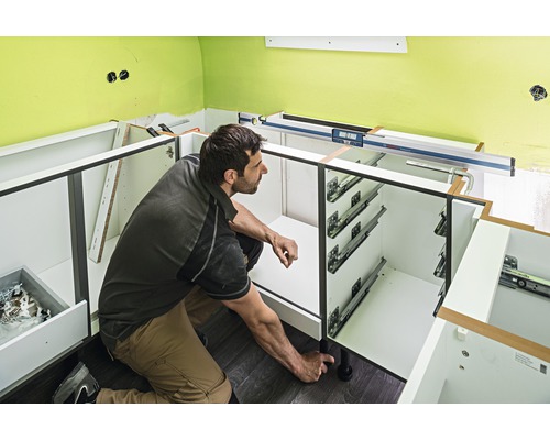 Muž montuje spodné kuchynské skrinky s výsuvmi a vyrovnávacími nožičkami.