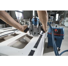 Muž pracuje s hornou frézou na drevenom obrobku, pripojenou k vysávaču.