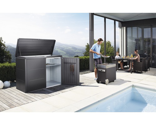 Záhradná scéna s domčekom na náradie, grilom a rodinou pri jedálenskom stole na terase