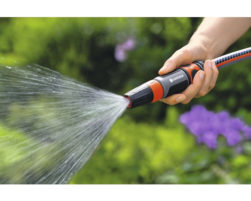 Osoba drží záhradnú hadicu s rozprašovacou tryskou, z ktorej vyteká voda.