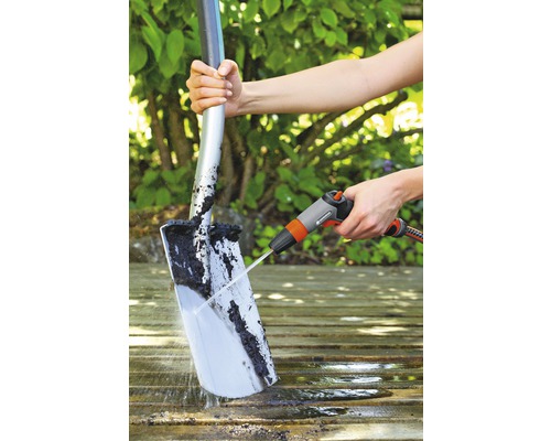 Osoba čistí lopatu prúdom vody na drevenom povrchu.