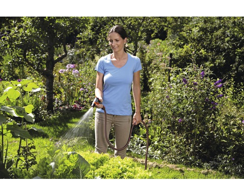 Žena zavlažuje záhradu záhradnou hadicou a striekacou pištoľou