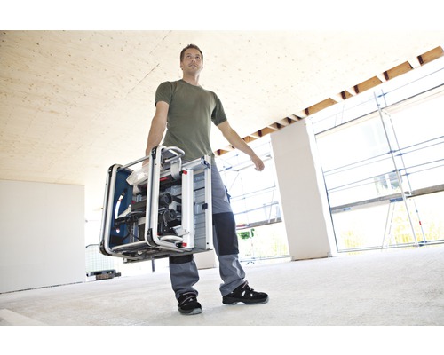 Muž nesie stolovú kotúčovú pílu v miestnosti vo výstavbe.