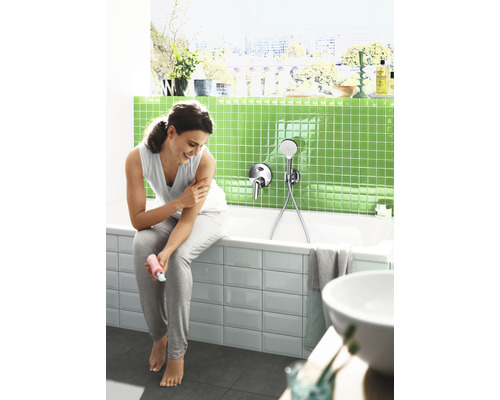 Svetlá kúpeľňa s vaňou, batériou a ženou, ktorá sa natiera krémom.