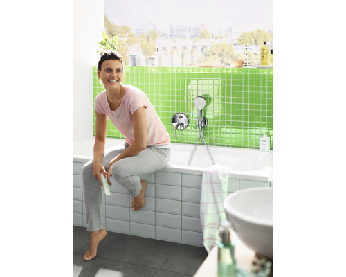 Žena sedí na okraji vane v kúpeľni s nástennou sprchovou súpravou.