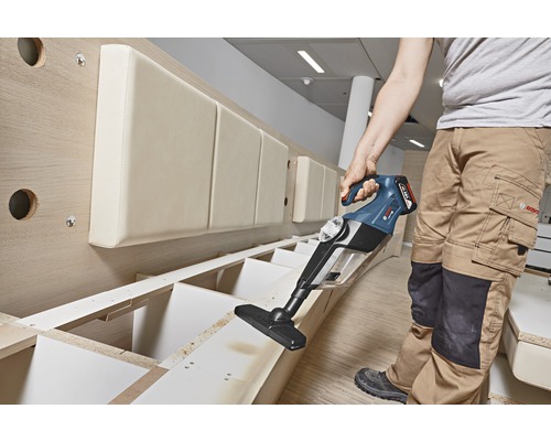 Osoba používa akumulátorový vysávač na čistenie drevenej police.