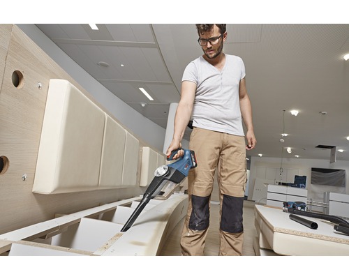 Muž vysáva piliny z kusu nábytku pomocou akumulátorového vysávača.