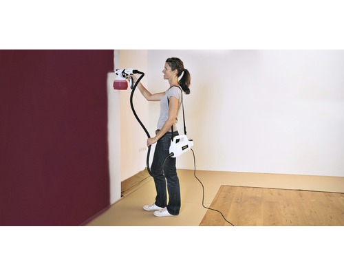 Žena maľuje stenu farbiacim striekacím systémom v miestnosti