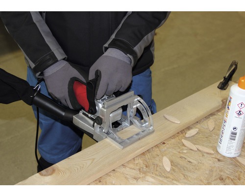 Remeselník používa lamelovaciu frézu na drevenej doske spolu s drevenými konektormi a lepidlom.