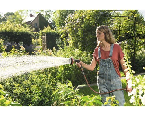 Žena polieva záhradu záhradnou hadicou a postrekovačom