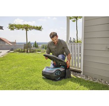 Muž otvára robotickú kosačku na trávu v záhrade.