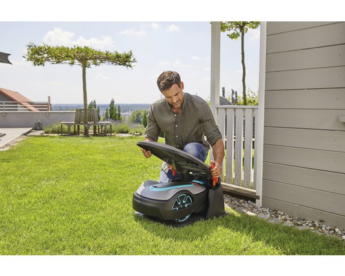 Muž otvára robotickú kosačku na trávu v záhrade.