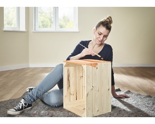 Žena natiera drevenú debnu štetcom a farbou