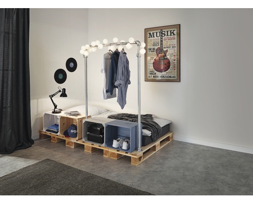 Spálňa s posteľou z drevených paliet, zdobená svetelnou reťazou a hudobným plagátom