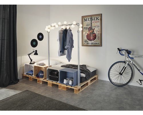 Spálňa s paletovou posteľou, vešiak na šaty s osvetlením a ozdobné debny