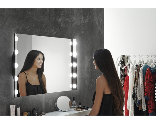 Žena pred osvetleným kozmetickým zrkadlom v kúpeľni.