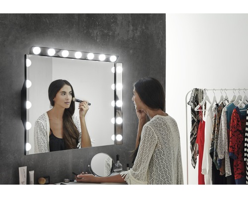 LED svetlo nad zrkadlo Focco E27135CI/C0250 Hollywood S3 IP44 2,7 W 1113 lm čierne Žena pred osvetleným kozmetickým zrkadlom s výberom make-up produktov na stole
