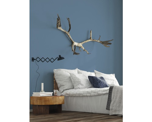 Spálňa s posteľou, nočným stolíkom, lampou a parožím na stene.