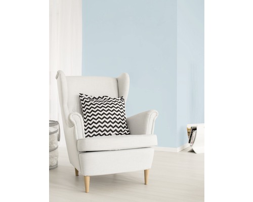 Svetlá obývacia izba s pastelovou modrou farbou stien, bielym kreslom a vankúšom s cikcakovým vzorom