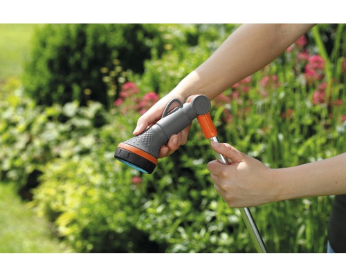 Záhradná hadica so sprchovou hlavicou v ruke pred zelenými rastlinami