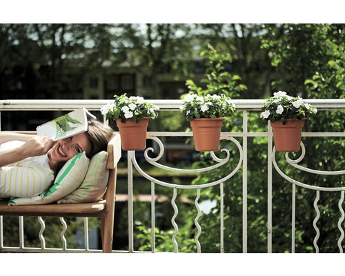 Žena relaxuje na lavičke na balkóne s kvetináčmi na zábradlí