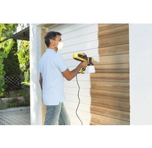 Muž lakuje drevenú stenu pomocou systému na striekanie farieb