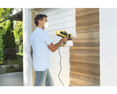 Muž lakuje drevenú stenu pomocou systému na striekanie farieb