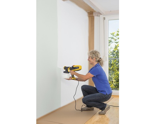 Žena používa striekací systém na farby na vnútorné steny.