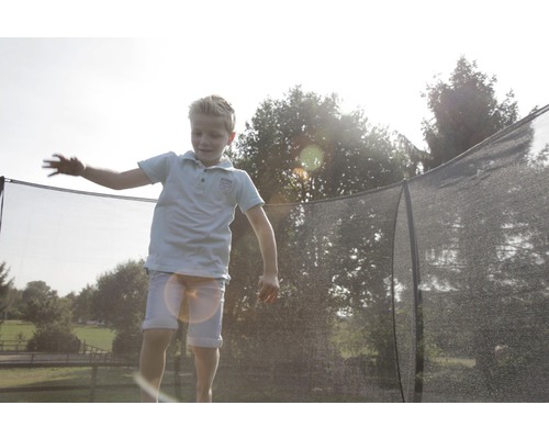 Dieťa skáče na záhradnej trampolíne s bezpečnostnou sieťou.