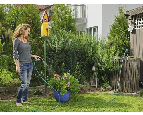 Žena polieva kvety záhradnou hadicou v záhrade.