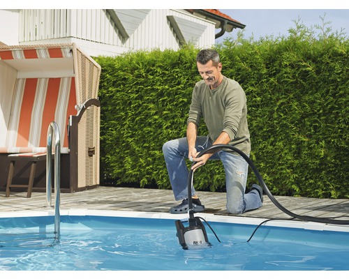 Muž obsluhuje ponorné čerpadlo na vypúšťanie bazéna v záhrade.