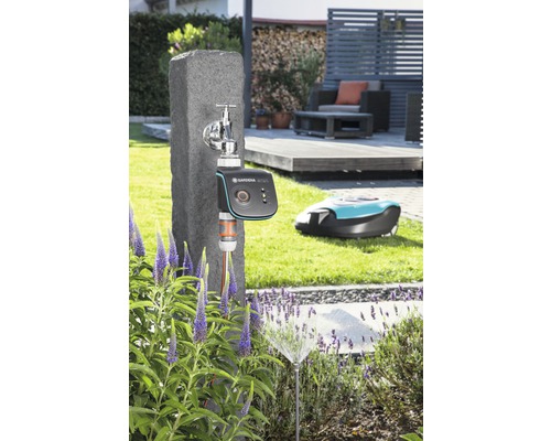 Scéna s vodovodným kohútikom, zavlažovacím počítačom Gardena, zavlažovačom trávnika a robotickou kosačkou v záhrade.