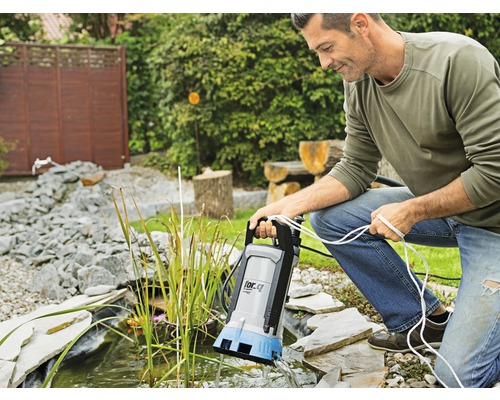 Muž obsluhuje jazierkové čerpadlo pri záhradnom jazierku.