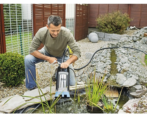 Muž obsluhuje jazierkové čerpadlo na okraji záhradného jazierka, ktoré je obklopené kameňmi.