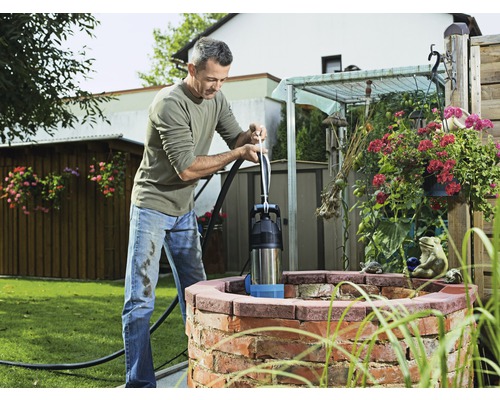 Muž obsluhuje ručnú piestovú pumpu pri studni v záhrade.